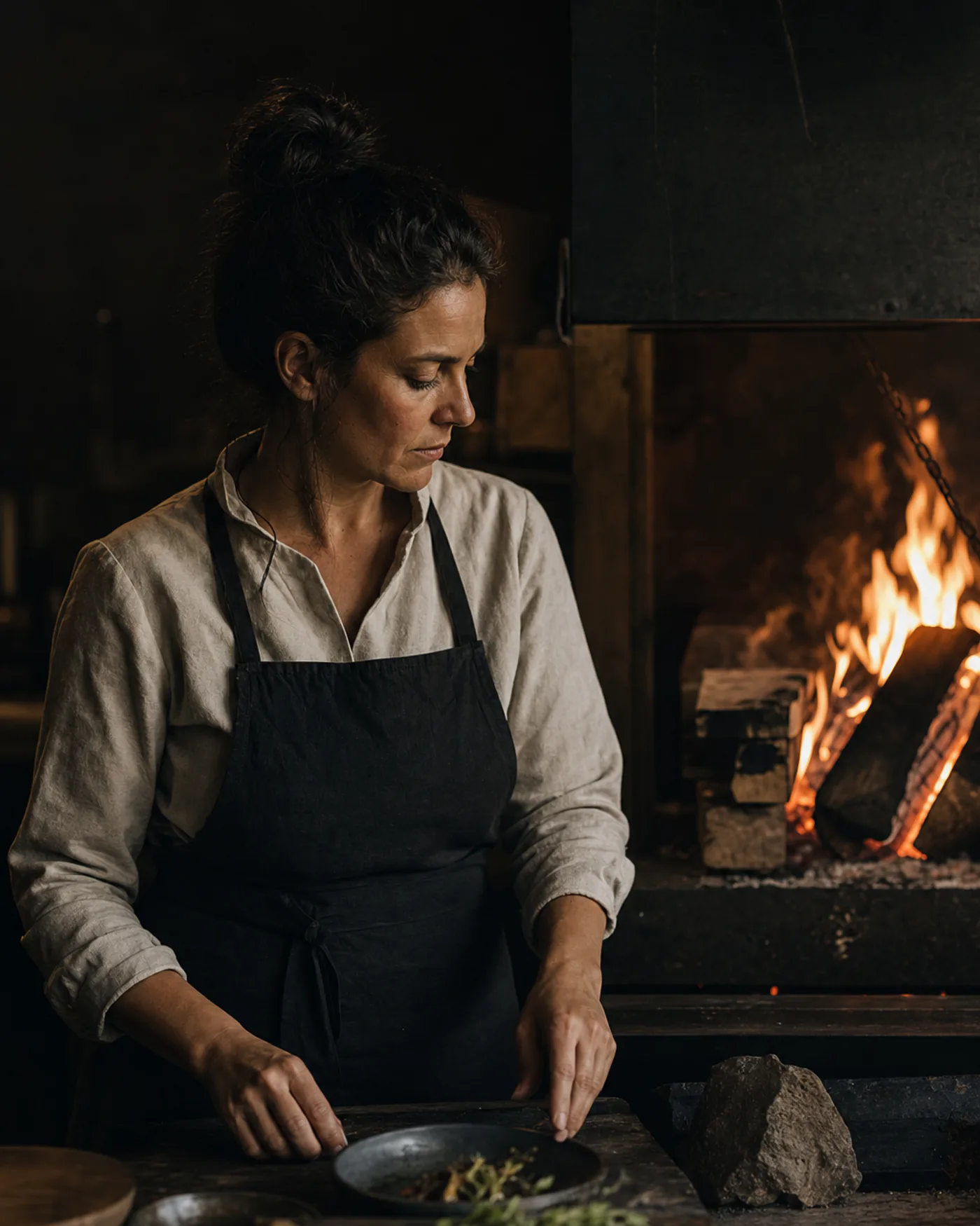 Chef Mara Voss working beside the live fire in the EMBER & SALT kitchen.